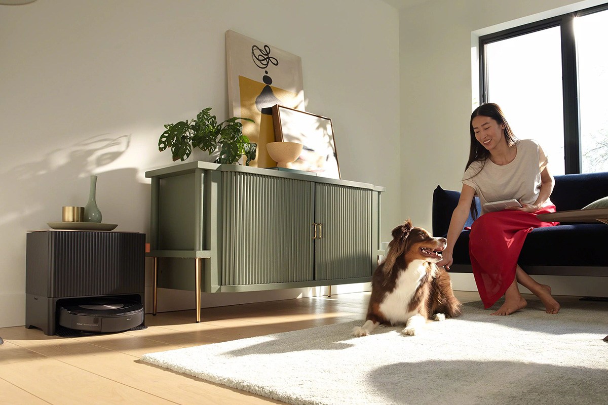 Roomba Combo j9+on clean base next to woman sitting on sofa petting dog