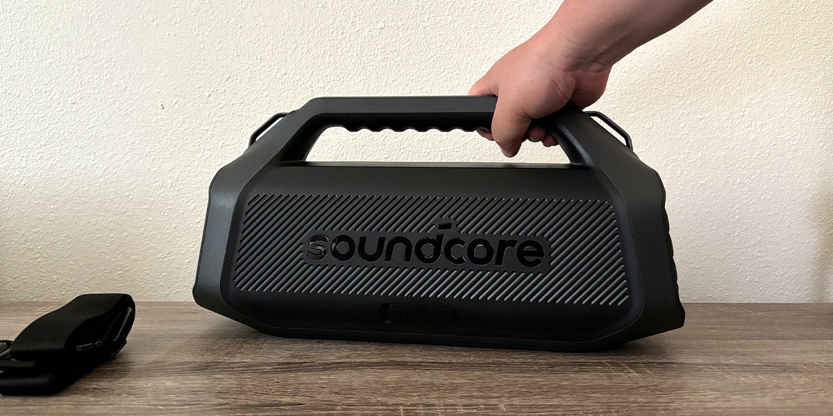 Soundcore Boom 2 Plus Outdoor on table with hand on carrying handle
