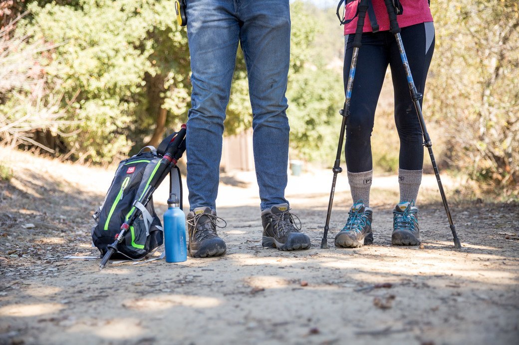 Two people, one wearing jeans and the other wearing black leggings, pause for a rest while hiking.