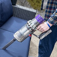 Person vacuuming outdoor sofa with cordless vacuum